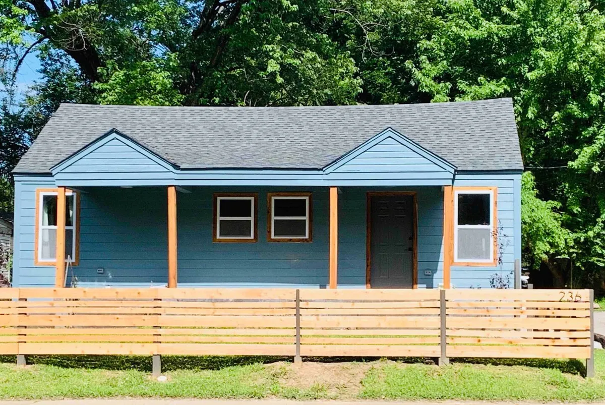 This image shows the blue exterior of the house, complemented by a wooden fence and a welcoming front porch. The porch provides a glimpse of a relaxing sitting area, while the yard in front is well-kept, suggesting a safe and inviting entryway.