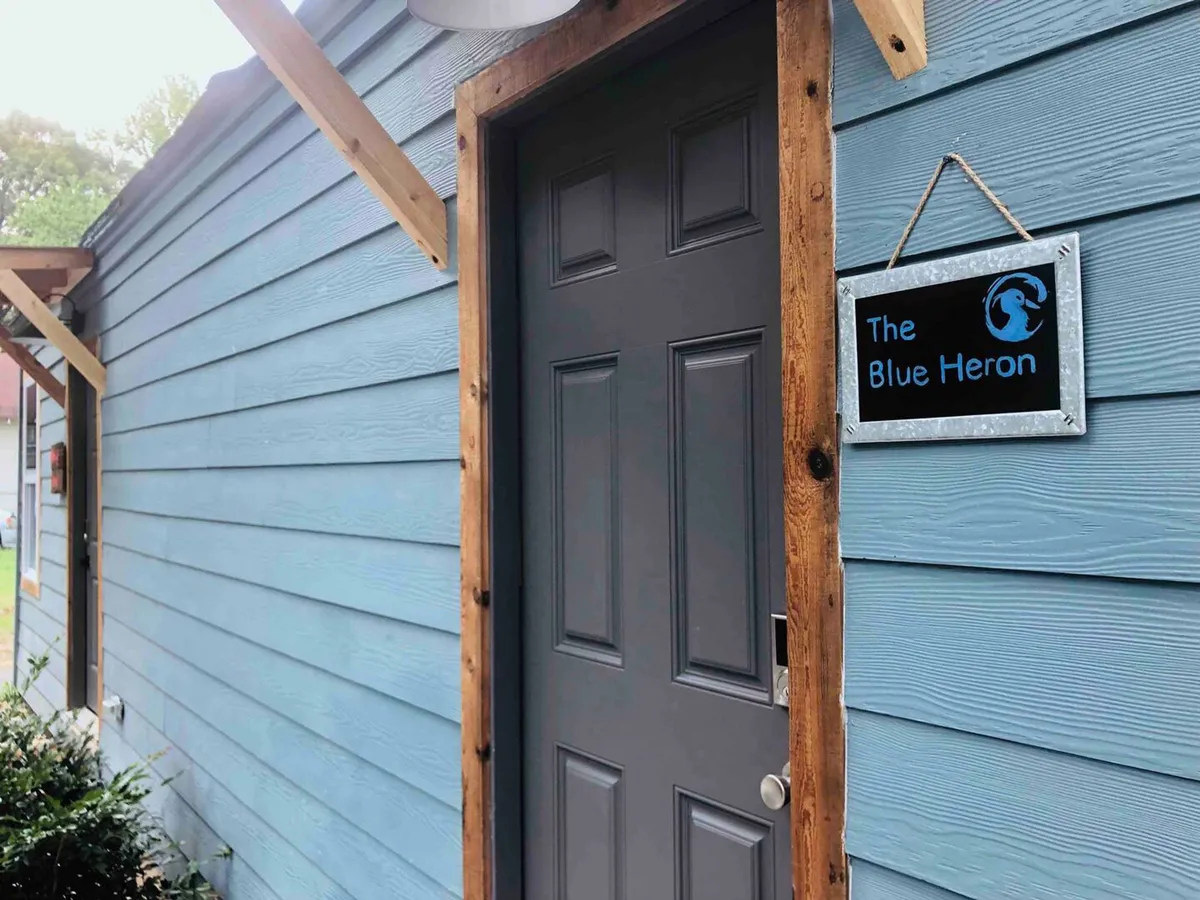 This image captures the inviting entrance of The Blue Heron, featuring a prominent sign, a gray door, and a wooden frame. The scene reinforces a warm welcome and hints at the cozy atmosphere that awaits inside. Guests can imagine themselves arriving and starting their business or leisure trip in a friendly, comfortable setting.