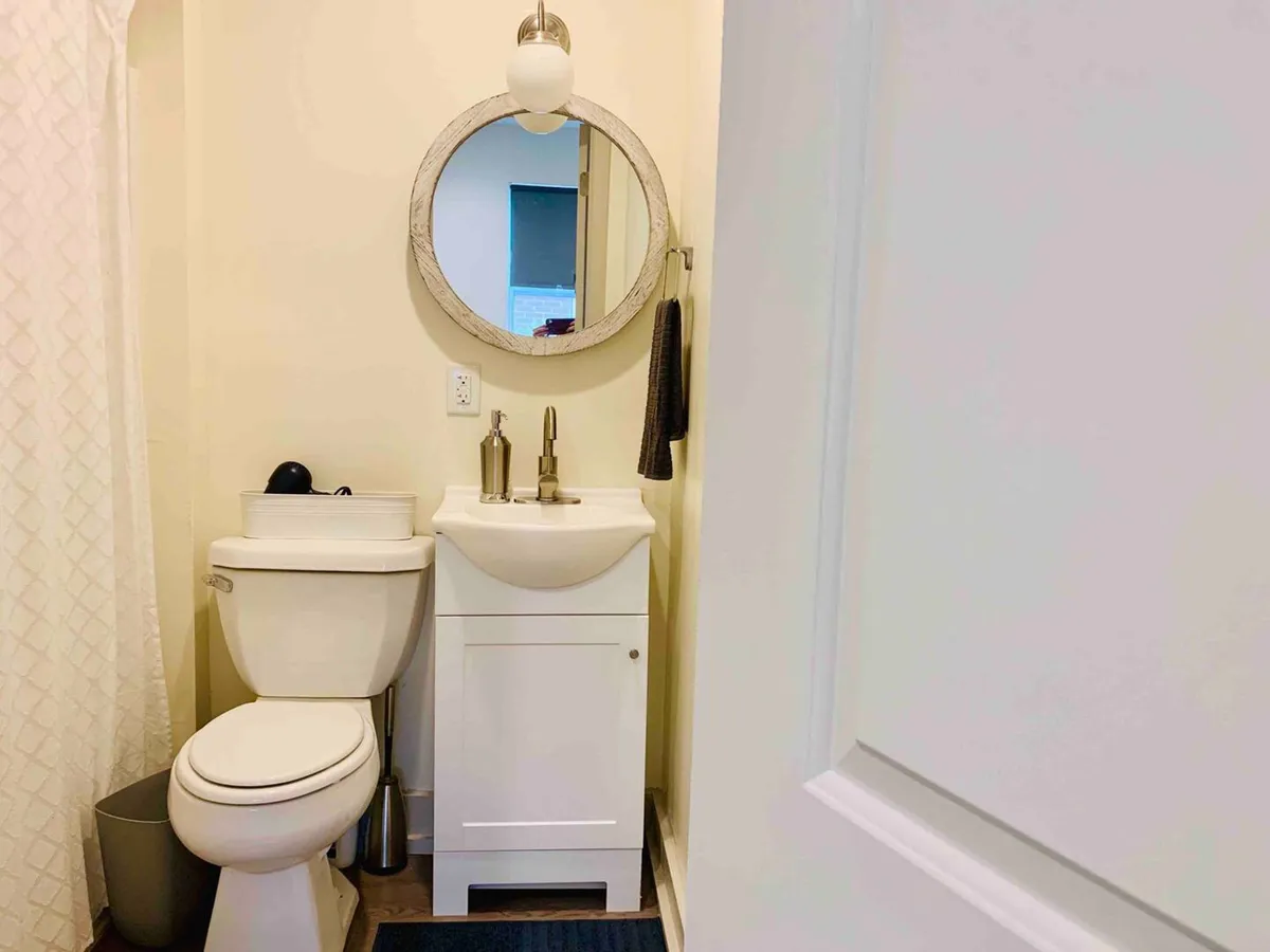 A clean, private bathroom with a round mirror above the sink, a modern faucet, toilet, and neatly arranged towel holder. The space feels fresh and inviting, embodying a sense of cleanliness and personal comfort.