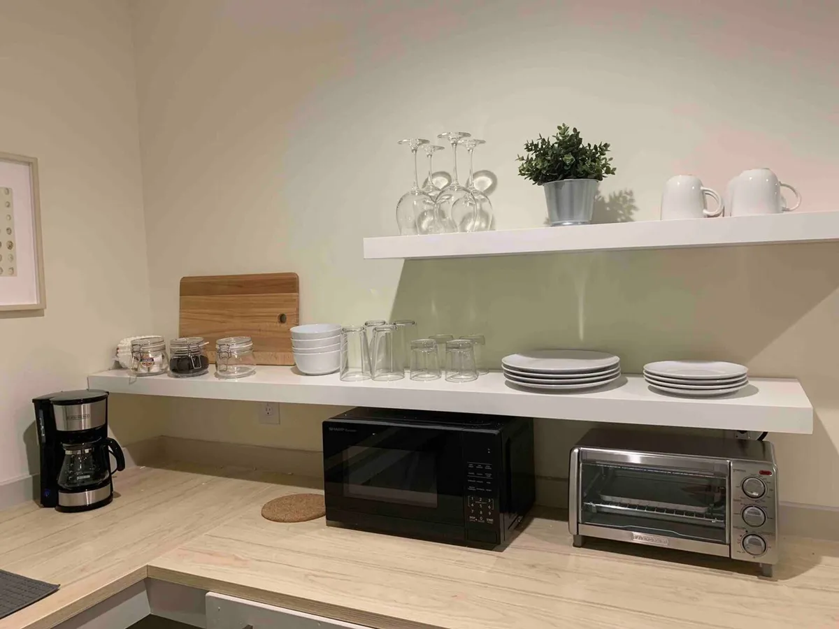 A welcoming, modern kitchen area with a prominent coffee maker, microwave, dishes, glassware, and a small plant. The space feels functional yet inviting, equipped for meal preparation or enjoying a first cup of coffee in the morning.