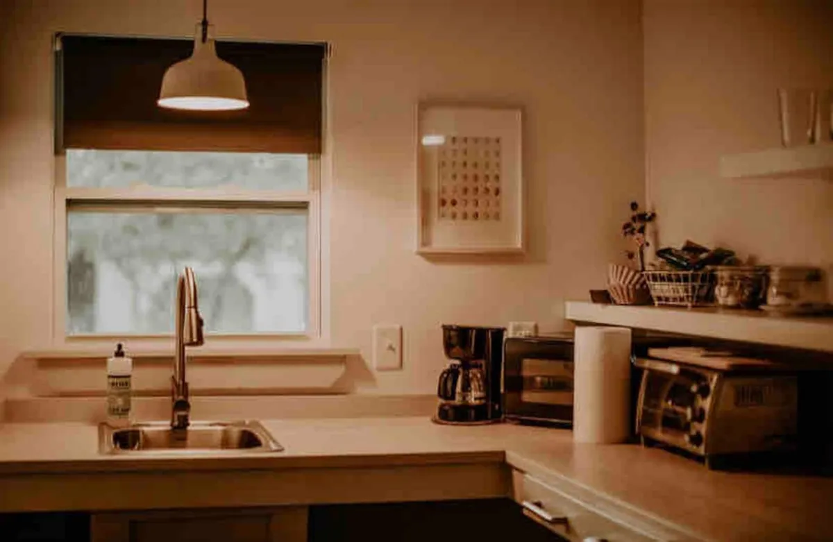 A kitchen area with a coffee maker, toaster, and kitchen sink by a sunlit window, creating a warm and inviting atmosphere. The scene suggests the enjoyment of a fresh cup of coffee and the convenience of having refreshments close to the living area.