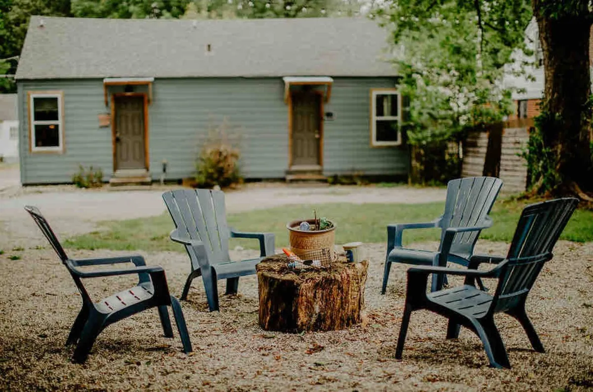 This exterior shot features a cozy fire pit surrounded by Adirondack chairs and lush greenery. The setting suggests a communal, yet private outdoor space ideal for relaxing, having coffee, or unwinding in the evening.